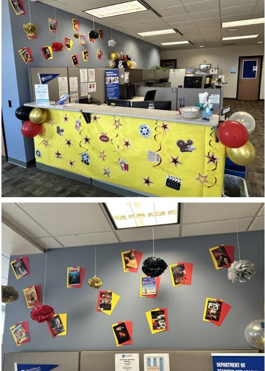 Front desk is decorated with yellow banner and move decorations. There are red and gold and black balloons with pom poms hanging from the ceiling. There are mini movie posters covering the wall